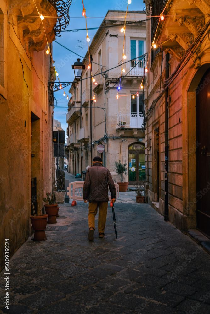 Elderly man walking in illuminated alley in Ortigia