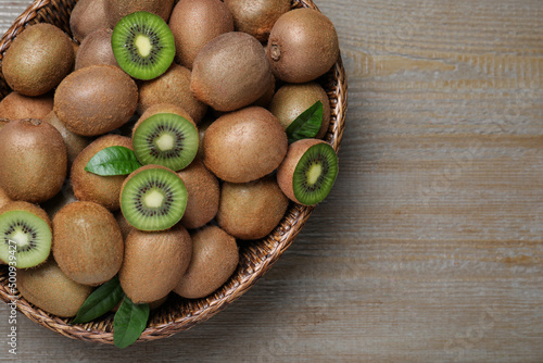 Fresh ripe kiwis in wicker bowl on wooden table, top view. Space for text