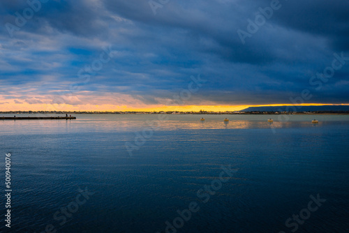 Sunset over the sea with cloudy sky and small harbor with people
