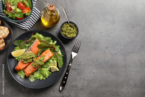Tasty cooked salmon with pesto sauce served on dark grey table, flat lay. Space for text