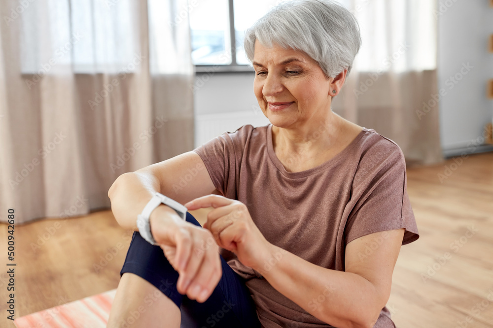 © Syda Productions - sport, fitness and healthy lifestyle concept - smiling senior woman with smart watch or tracker exercising at home