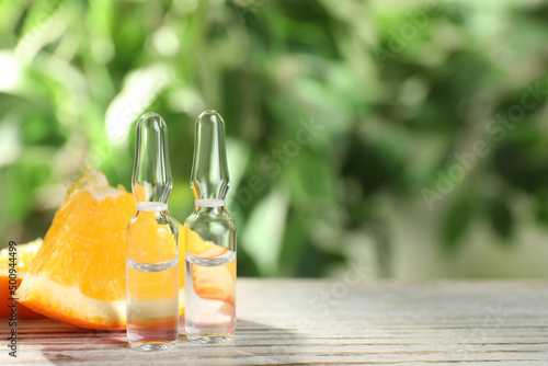 Pharmaceutical ampoules with medication and orange slices on white wooden table, space for text