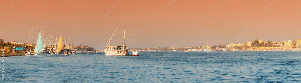 Panoramic view of traditional Egyptian ferry boats and cruise ships down the Nile with ancient temples of Luxor in the background