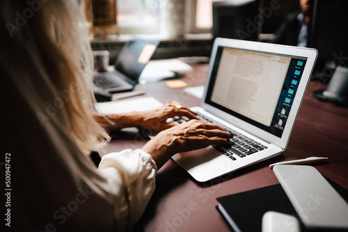 Midsection of female lawyer using laptop while typing at desk in office photo