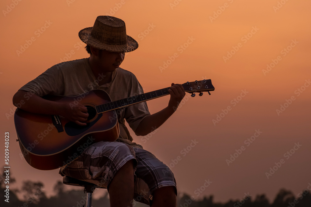 Fototapeta premium Close-up of man in hat playing guitar at sunset