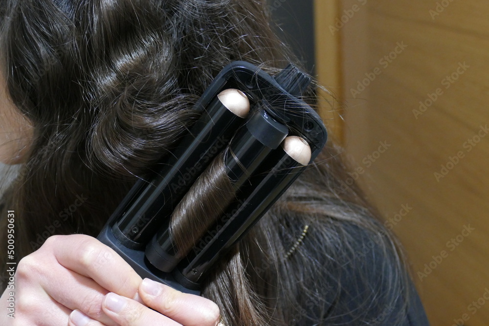 Fototapeta premium Mujer realizando ondas en su pelo negro. Ondulador de pelo