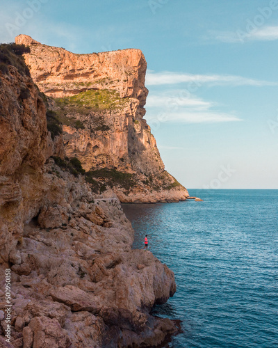 Foto área de paisaje de acantilados y mar, con persona de silueta. Foto en vertical.