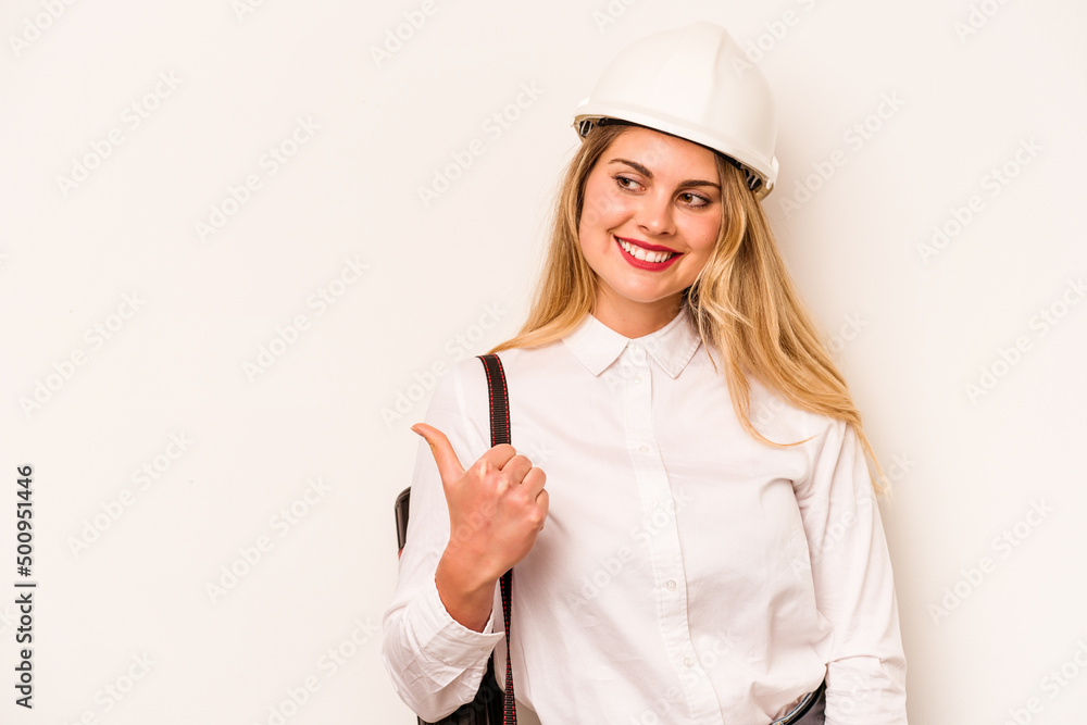 Young architect woman with helmet and holding blueprints isolated on white background points with thumb finger away, laughing and carefree. Young architect woman with helmet and holding blueprints isolated on white background points with thumb finger away, laughing and carefree.