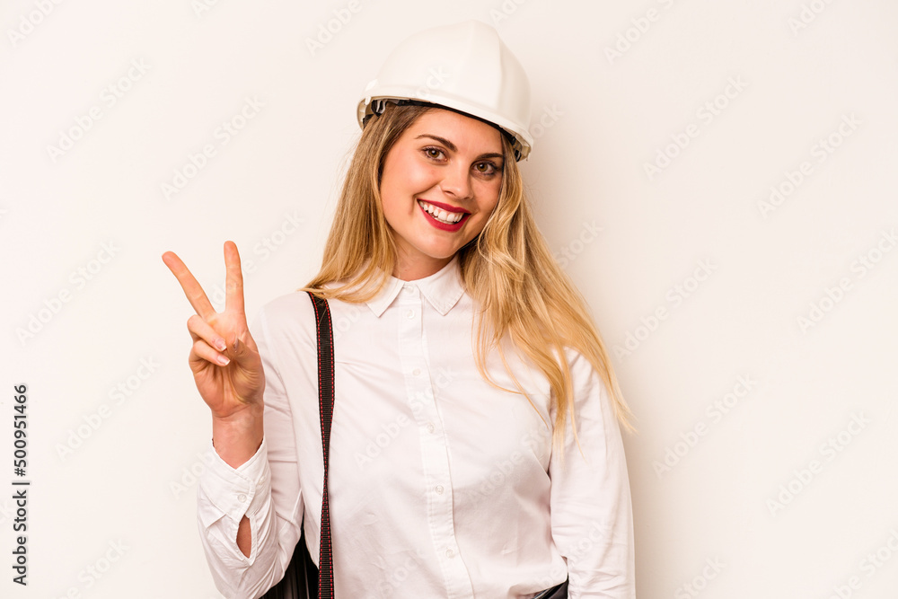 Young architect woman with helmet and holding blueprints isolated on white background joyful and carefree showing a peace symbol with fingers.