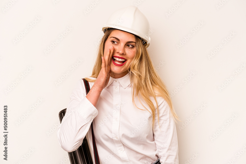 Young architect woman with helmet and holding blueprints isolated on white background shouting and holding palm near opened mouth.