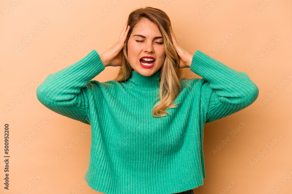 Young caucasian woman isolated on beige background covering ears with hands trying not to hear too loud sound. Young caucasian woman isolated on beige background covering ears with hands trying not to hear too loud sound.