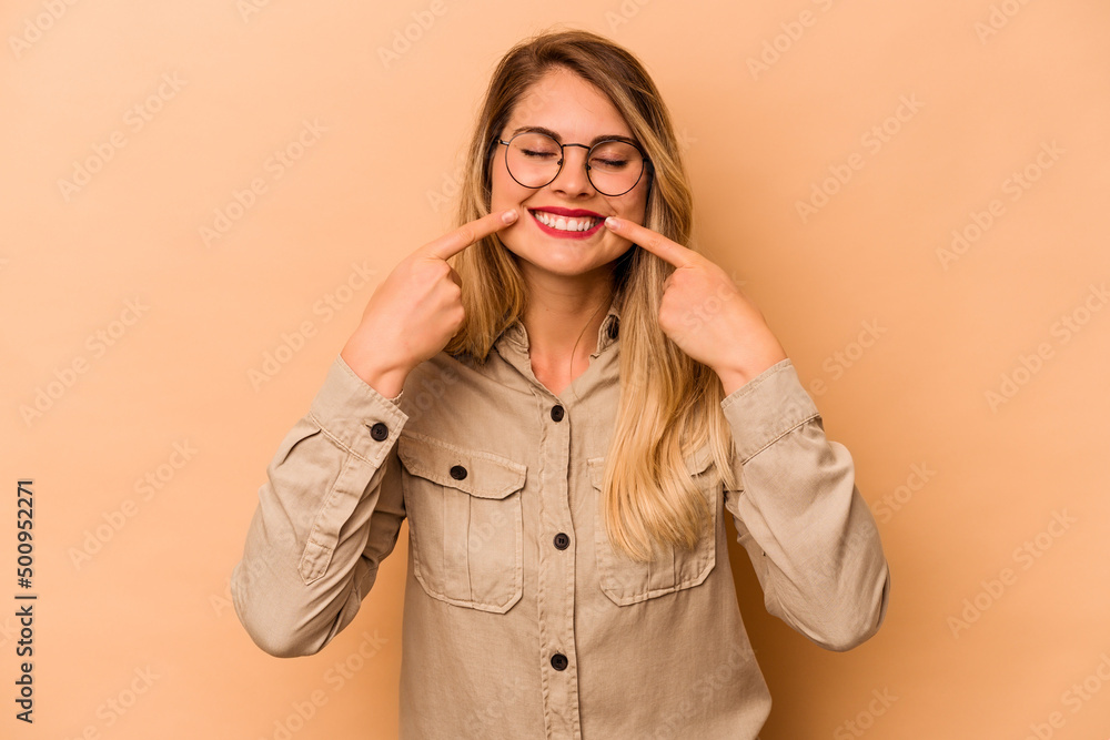 Young caucasian woman isolated on beige background smiles, pointing fingers at mouth.