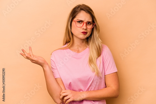 Young caucasian woman isolated on beige background doubting and shrugging shoulders in questioning gesture.