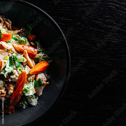 Chicken, carrot, lettice salad in plate on black background photo