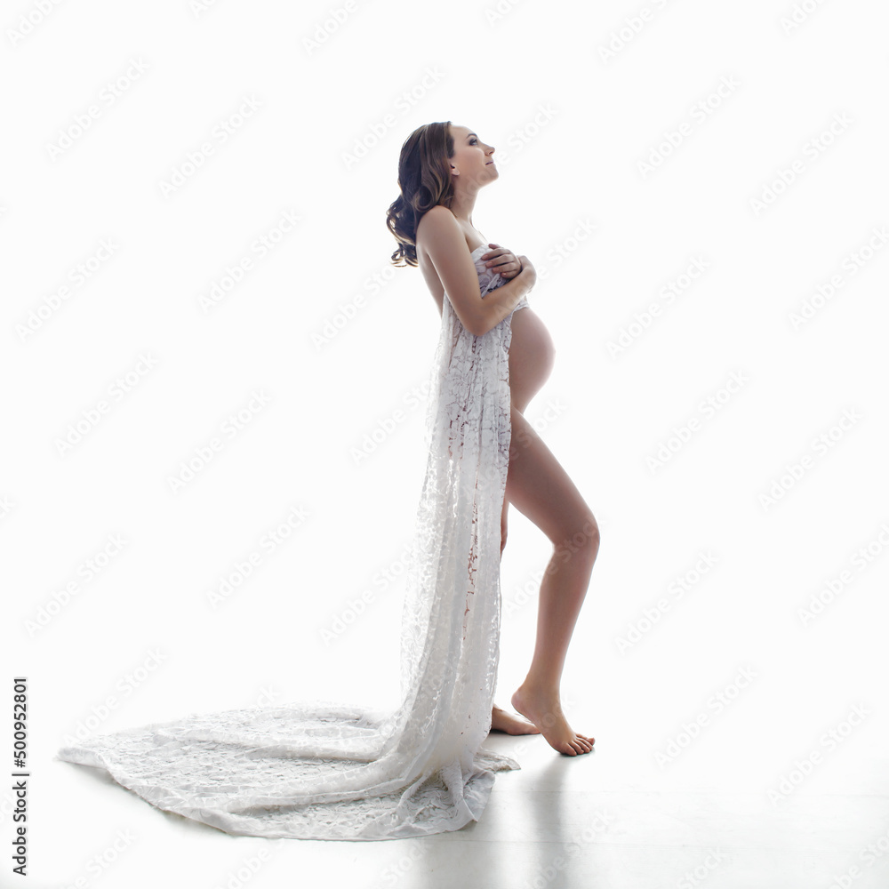 Naklejka premium Pregnant woman in white lace lingerie posing at photostudio on white background