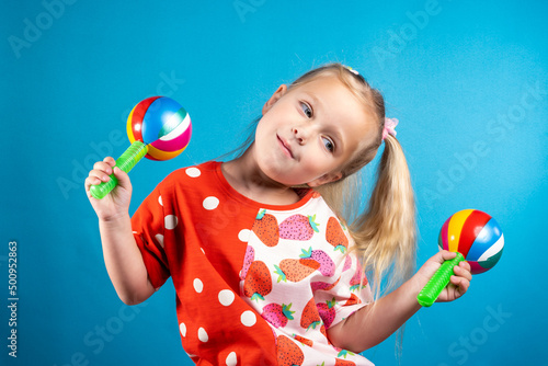 A cute girl in red is dancing with maracas. The concept of children's creativity, the development of musical abilities, gifted children, preschool education, fun pastime.