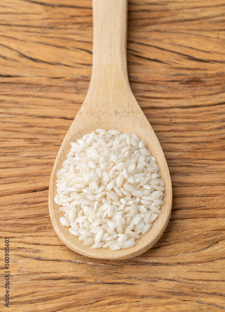 Raw carnaroli risotto rice on a spoon over wooden table Raw carnaroli risotto rice on a spoon over wooden table