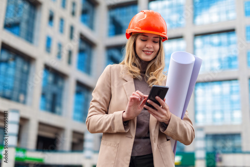 Women architectural engineers portrait. Engineer woman using phone and holding plans