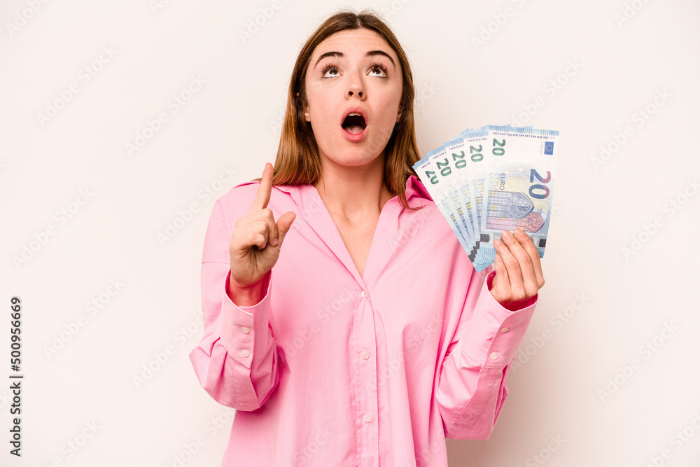 Young woman holding banknotes isolated on white background pointing upside with opened mouth. Young woman holding banknotes isolated on white background pointing upside with opened mouth.