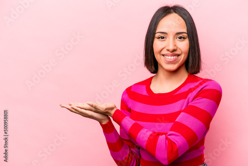 Young hispanic woman isolated on pink background holding a copy space on a palm. © Asier