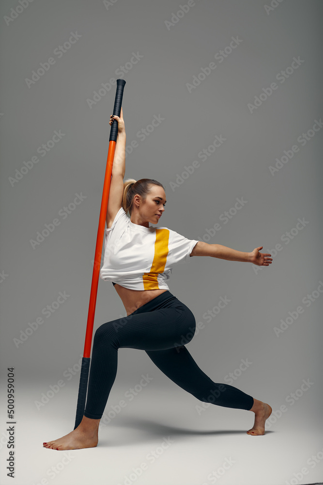 beautiful girl in sports uniform is training kung fu in the studio, fighter athlete, practicing martial arts with a stick