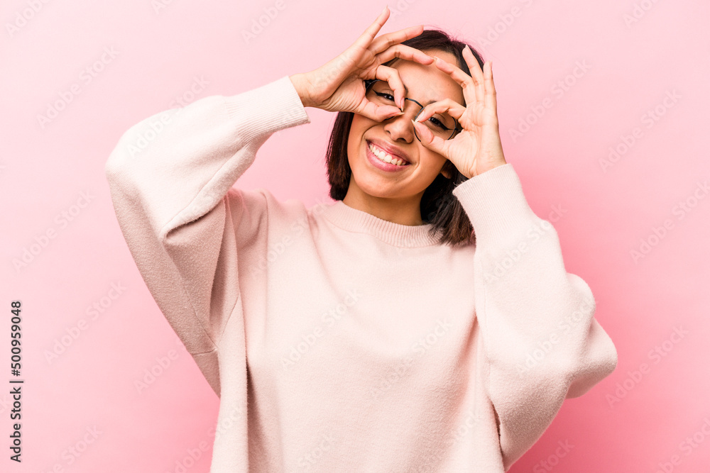 Young hispanic woman isolated on pink background showing okay sign over eyes Young hispanic woman isolated on pink background showing okay sign over eyes