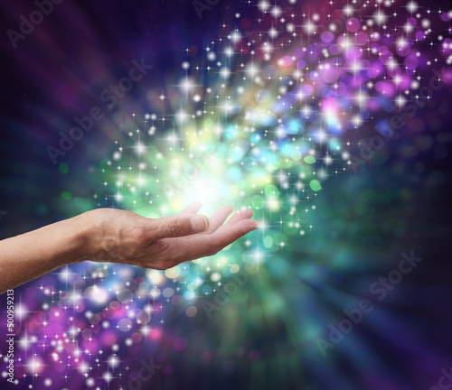 Magical Energy Healing Hands Concept - sparkling and bokeh background with a female open palm in the middle and a stream of multicoloured energy flowing through a subtle spiral 