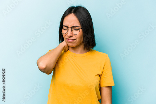 Young hispanic woman isolated on blue background having a neck pain due to stress, massaging and touching it with hand. © Asier