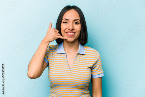 Young hispanic woman isolated on blue background showing a mobile phone call gesture with fingers.