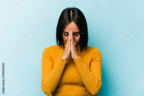 Canvas Young hispanic woman isolated on blue background praying, showing devotion, religious person looking for divine inspiration
