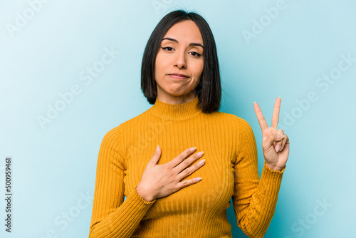 Photography Young hispanic woman isolated on blue background taking an oath, putting hand on chest