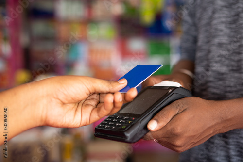 Close up shot of customer paying money by tapping credit card to swiping machine at grocery shop - concept of digital payment, contact less transaction, and safety