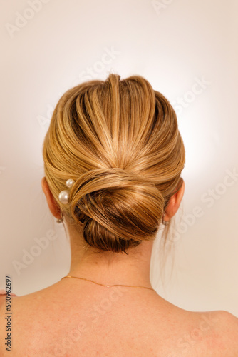 The concept of style, style and beauty. An isolated shot of a girl from behind with blonde hair gathered in a neat bun at the back of her head, against a white studio background. A hairstyle for girls
