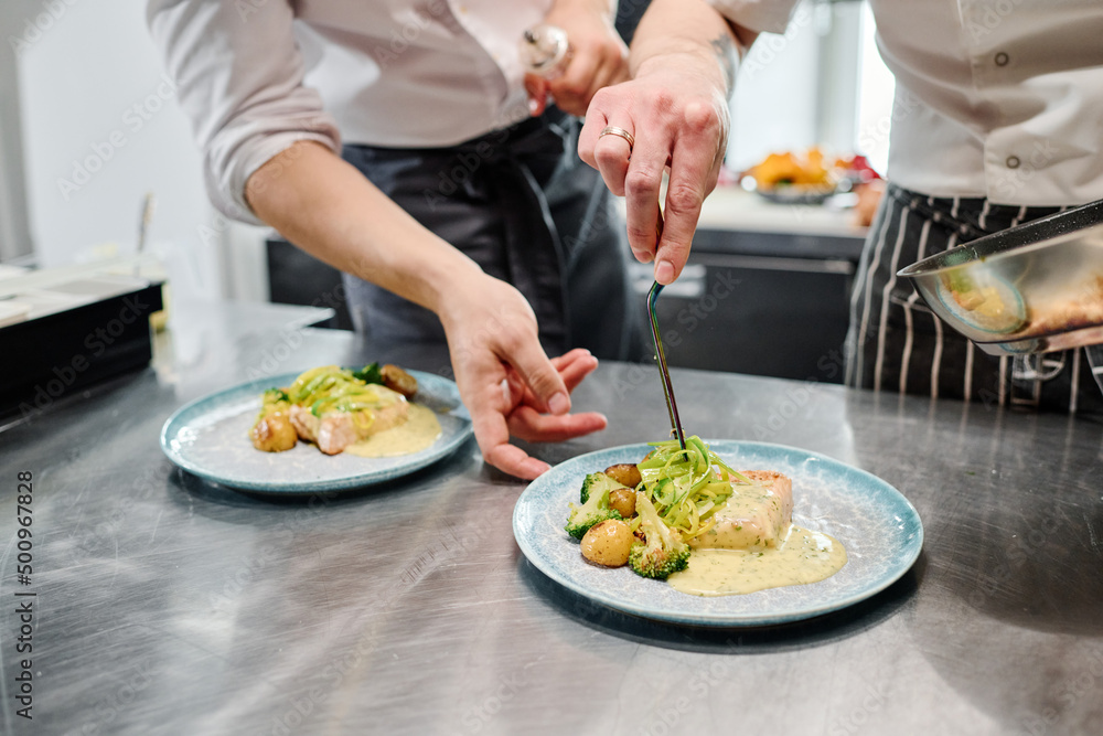 Close-up of assistant learning to decorate dish with salad with chef teaching him in kitchen Close-up of assistant learning to decorate dish with salad with chef teaching him in kitchen