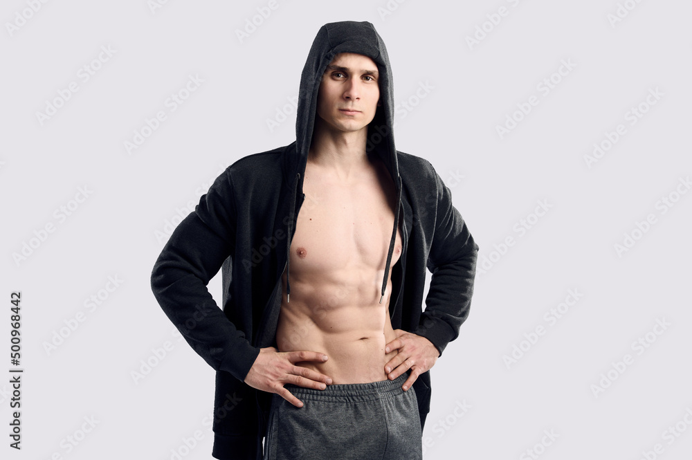 Strong caucasian muscular fitness model body abs posing. Brutal bodybuilder fitness model posing on gray background. Fitness man wearing hoodie on naked body. Strong caucasian muscular fitness model body abs posing. Brutal bodybuilder fitness model posing on gray background. Fitness man wearing hoodie on naked body.