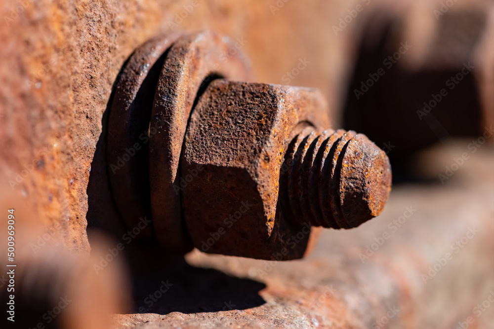 Rusty corroded iron screw with washer and thread horizontal on a railway profile. Monochrome orange brown metal surface of a hex nut fixing. Macro close up with selective focus. Rusty corroded iron screw with washer and thread horizontal on a railway profile. Monochrome orange brown metal surface of a hex nut fixing. Macro close up with selective focus.