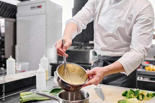 Murais de parede Close-up of chef in uniform pouring cream from bowl into saucepan to prepare cak