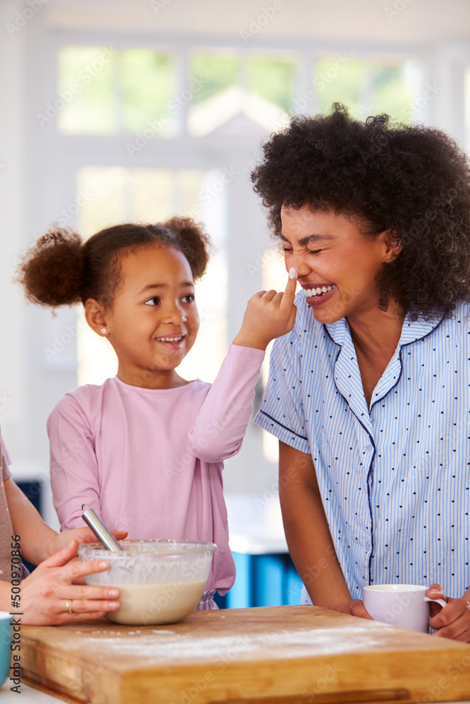 Family With Two Mums Wearing Pyjamas Making Morning Pancakes In Kitchen At Home With Daughter Family With Two Mums Wearing Pyjamas Making Morning Pancakes In Kitchen At Home With Daughter