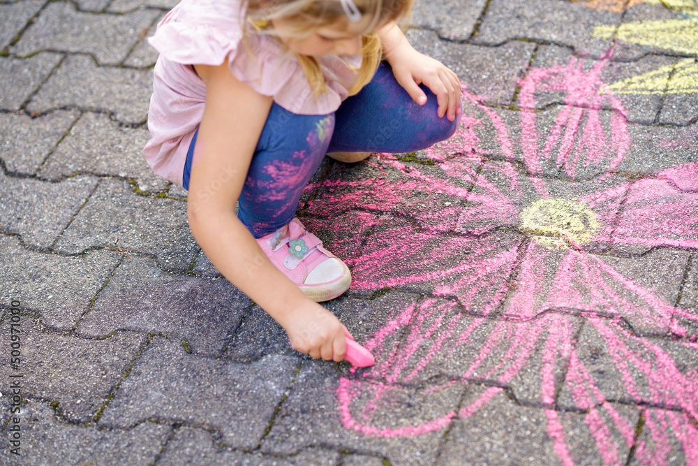 Little preschool girl painting with colorful chalks flowers on ground ...