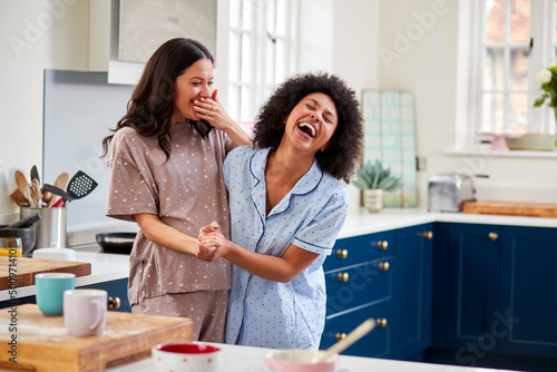 Loving Same Sex Pregnant Female Couple Wearing Pyjamas Dancing In Kitchen At Home