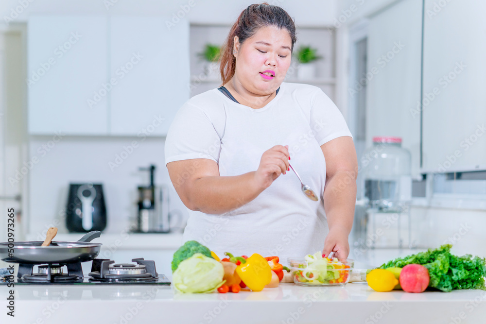 Fat woman eating a bowl of healthy salad at home