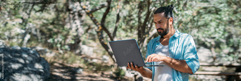 Male tourist working on a laptop outdoors in a camping.