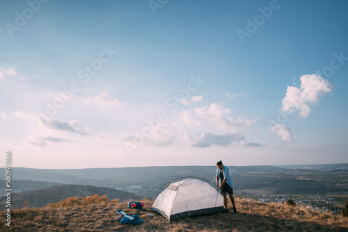 Young male tourist puts a tent in the mountains.