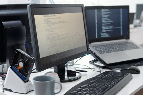 Computer monitor with decoded data on screen and laptop of contemporary programmers in openspace office or bureau