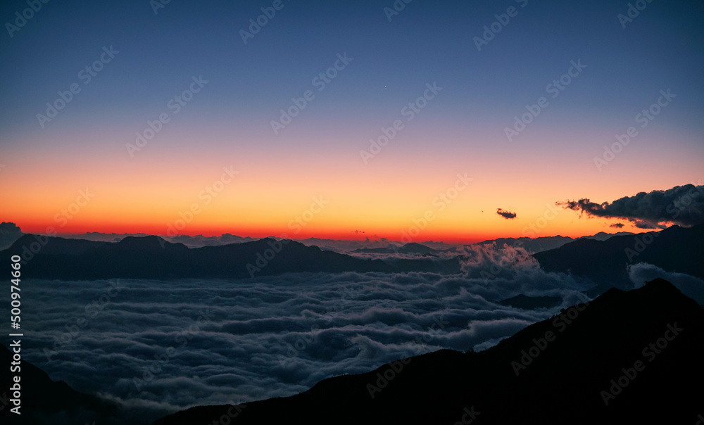 High angle shot of a sea of clouds at dawn viewed from a mountain top after a long trek. A silhouette scene that provokes calmness, positive vibe, mindfulness and suitable for text background.