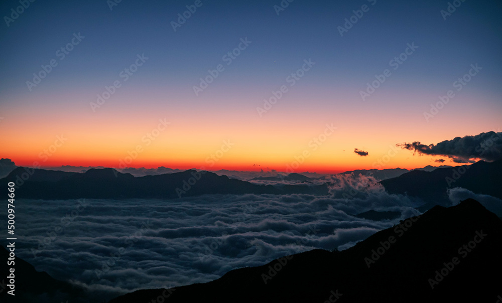 High angle shot of a sea of clouds at dawn viewed from a mountain top after a long trek. A silhouette scene that provokes calmness, positive vibe, mindfulness and suitable for text background. High angle shot of a sea of clouds at dawn viewed from a mountain top after a long trek. A silhouette scene that provokes calmness, positive vibe, mindfulness and suitable for text background.