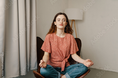 young woman sitting in a yoga pose in a leather chair and has her eyes closed