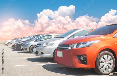Car parked in large asphalt parking lot in a row with white cloud and blue sky background. Outdoor parking lot