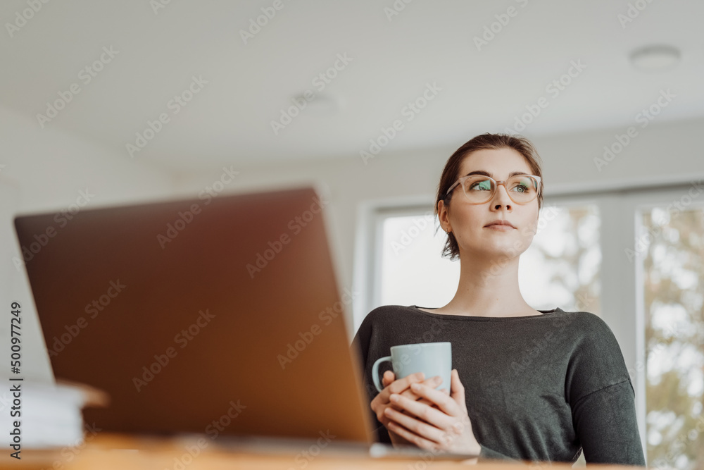 young thoughtful woman sits in living room with cup in hand and looks to the side young thoughtful woman sits in living room with cup in hand and looks to the side