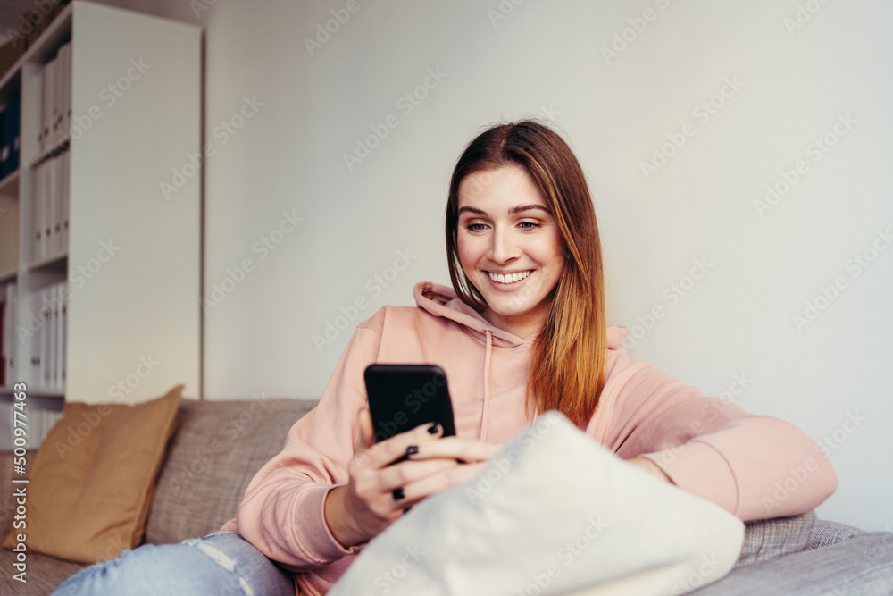 young woman sitting on a sofa and looking at her cell phone young woman sitting on a sofa and looking at her cell phone